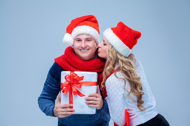 Bella coppia di Natale in cappelli di Babbo Natale che tiene presente su sfondo blu