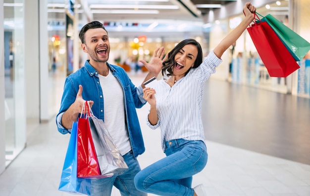 Bella coppia felice eccitata innamorata o famiglia con sacchetti di carta e carta di credito in mano mentre si cammina durante lo shopping nel centro commerciale