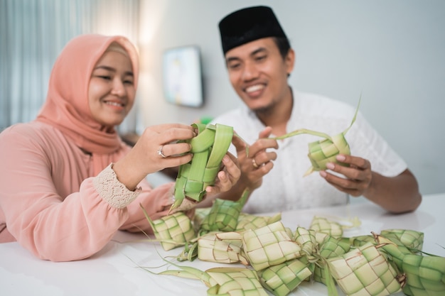 Bella coppia musulmana asiatica rendendo la torta di riso ketupat a casa utilizzando foglia di palma