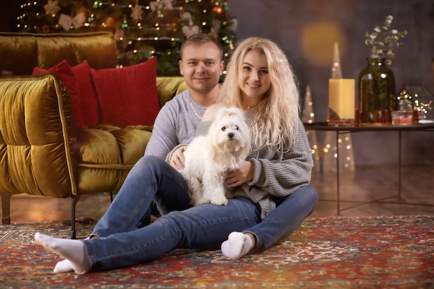 Bella coppia romantica con il loro cane vicino all'albero di Natale in un interno di casa accogliente estetico festivo Vero momento sincero Buon umore e divertirsi insieme Storia d'amore di Natale