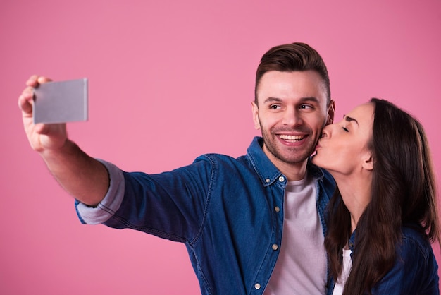 Bella coppia romantica isolata su sfondo rosa. La giovane donna attraente e l'uomo bello stanno facendo selfie, sorridendo e si divertono