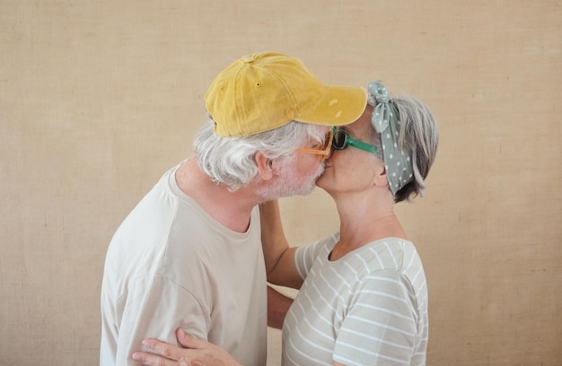 Bella coppia senior alla moda che abbraccia e bacia pensionati felici che esprimono affetto e amore