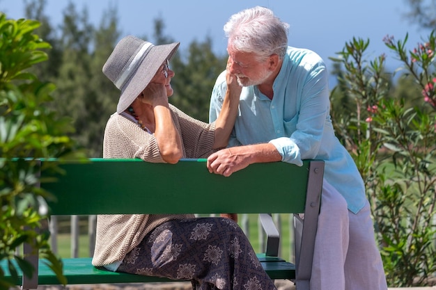 Bella coppia senior seduta all'aperto su una panchina del parco pubblico guardando negli occhi I nonni anziani sorridenti godono di uno stile di vita sano in una giornata di sole