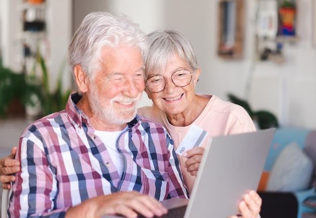 Bella coppia senior sorridente a casa navigando insieme sul computer portatile per lo shopping online