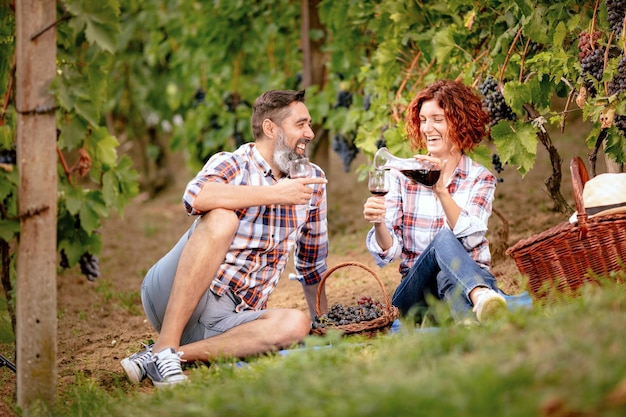 Bella coppia sorridente con picnic e degustazione di vino in un vigneto.