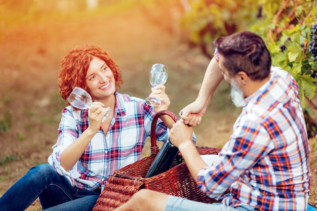 Bella coppia sorridente con picnic e degustazione di vino in un vigneto.