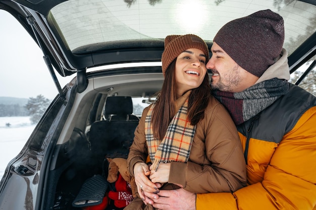 Bella coppia sorridente seduta nel bagagliaio di un'auto nella foresta invernale