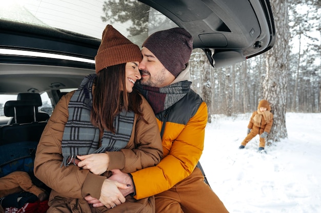 Bella coppia sorridente seduta nel bagagliaio di un'auto nella foresta invernale