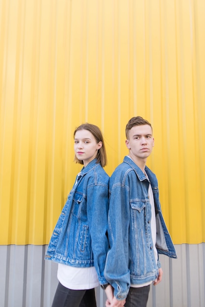 bella coppia vestita in giacche di jeans si trova sullo sfondo del muro giallo.