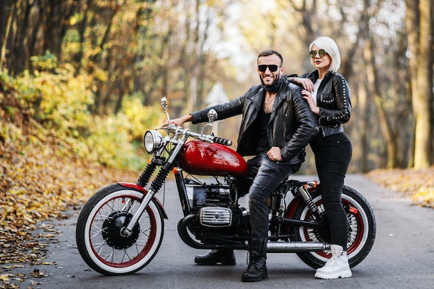 Bella coppia vicino alla moto rossa sulla strada nella foresta