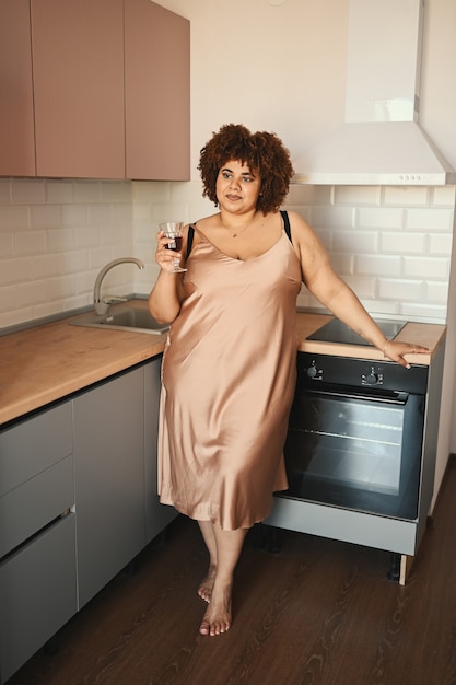 Bella curvy plus size donna nera africana capelli afro bere vino rosso su moderno scandinavo