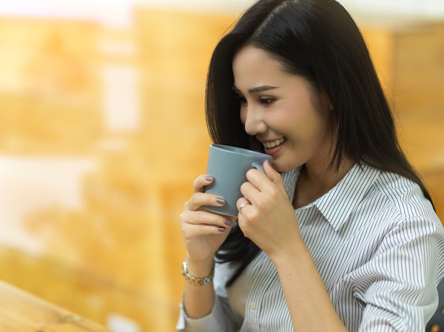 Bella dipendente beve caffè nella sua pausa caffè, donna che sorride e beve tè, vista laterale