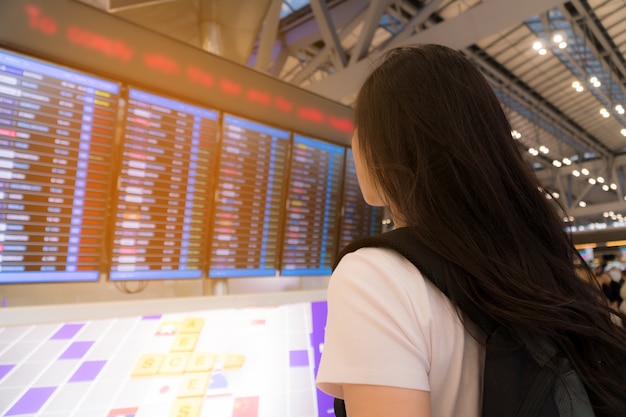 Bella donna a guardare l&#39;orario dei voli della sua partenza in aeroporto