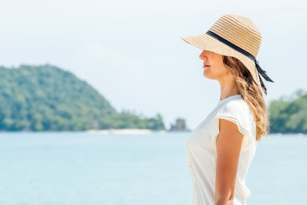 Bella donna abbronzata in abito bianco che copre il viso con un cappello di paglia