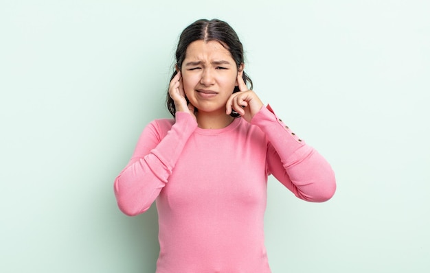 Bella donna adolescente che sembra arrabbiata, stressata e infastidita, coprendo entrambe le orecchie con un rumore assordante, un suono o una musica ad alto volume