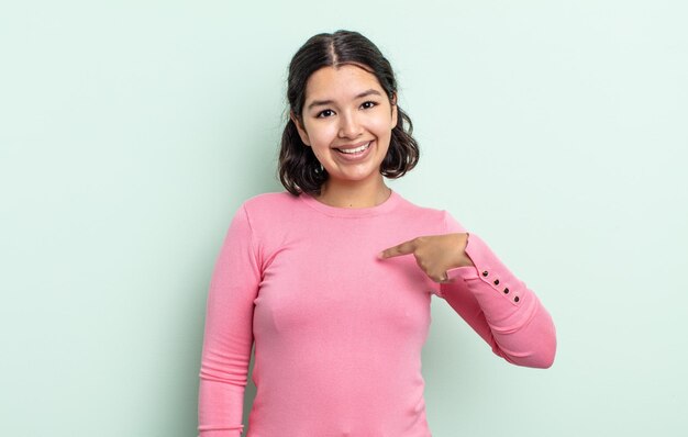 Bella donna adolescente che sembra felice, orgogliosa e sorpresa, indicando allegramente se stessa, sentendosi sicura e nobile