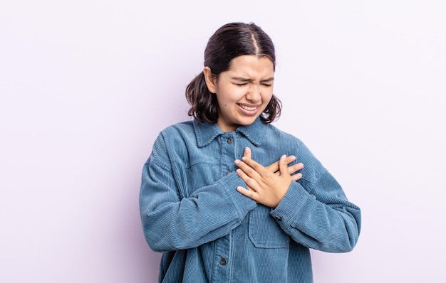 Bella donna adolescente che sembra triste, ferita e con il cuore spezzato, tenendo entrambe le mani vicino al cuore, piangendo e sentendosi depressa