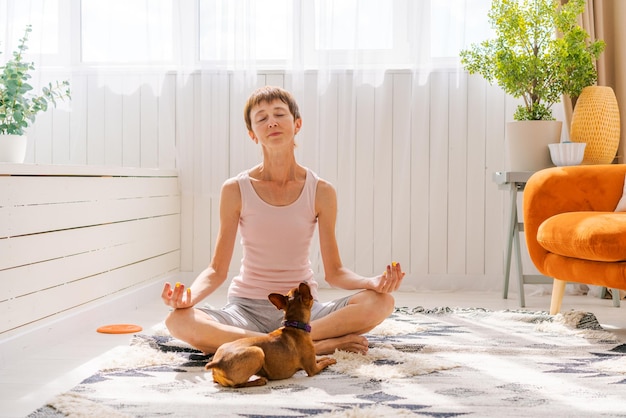 Bella donna adulta che pratica posa yoga con il cane pinscher pigmeo godendo