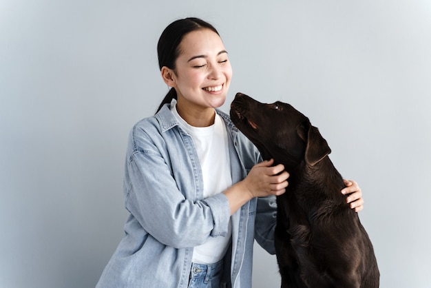 Bella donna affettuosa che accarezza un cane e ride su uno sfondo grigio