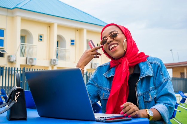 Bella donna africana entusiasta di ciò che ha visto sul suo laptop mentre tiene in mano la sua carta di credito.