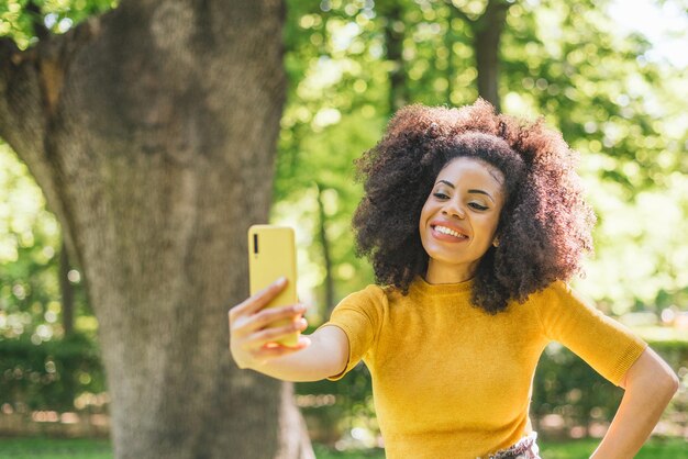 Bella donna afro che si fa un selfie sorridente nella foresta. Messa a fuoco selettiva.