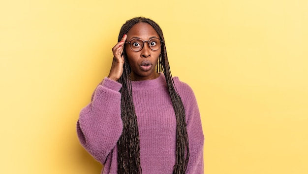 Bella donna afro nera che sembra sorpresa, a bocca aperta, scioccata, realizzando un nuovo pensiero, idea o concetto