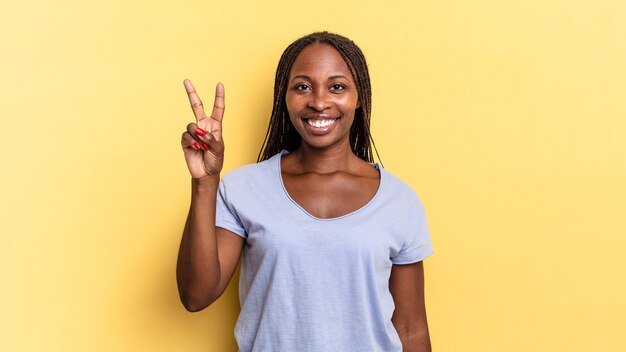 Bella donna afro nera che sorride e sembra amichevole, mostrando il numero due o il secondo con la mano in avanti, conto alla rovescia