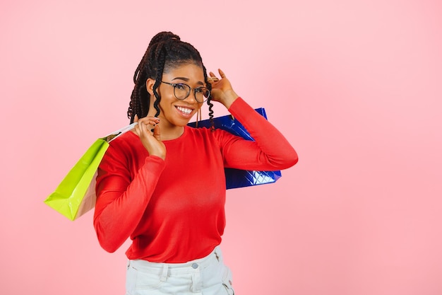 Bella donna afroamericana allegra con pile di sacchetti di carta in mano divertendosi godendosi lo shopping, isolata su sfondo rosa pastello.