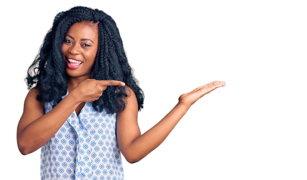 Bella donna afroamericana che indossa una camicia estiva casual stupita e sorridente alla telecamera mentre si presenta con la mano e indica con il dito.