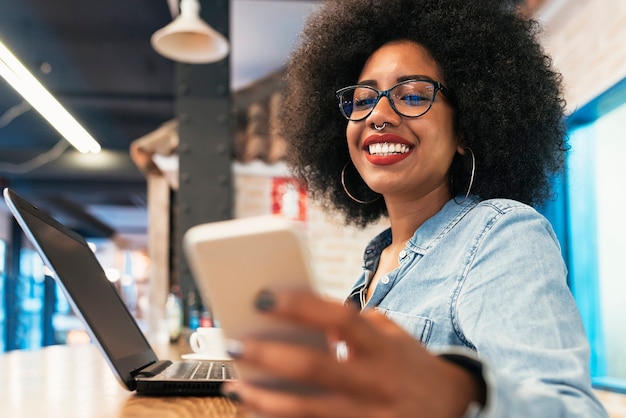 Bella donna afroamericana che utilizza il cellulare nella caffetteria. Concetto di comunicazione.