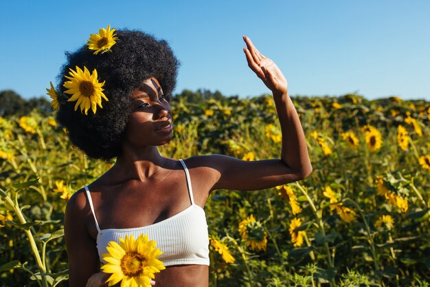 Bella donna afroamericana con capelli ricci stile afro in un campo di girasoli