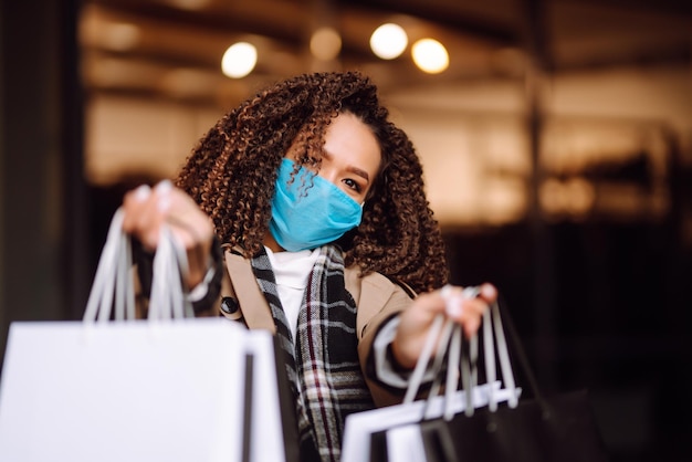 Bella donna afroamericana in maschera protettiva dopo lo shopping vicino al negozio