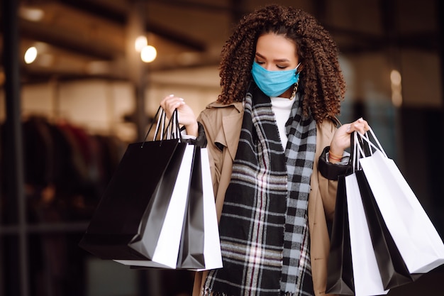 Bella donna afroamericana in maschera protettiva dopo lo shopping vicino al negozio