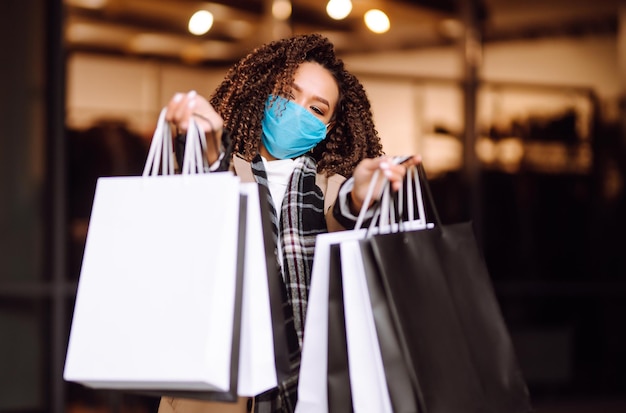 Bella donna afroamericana in maschera protettiva dopo lo shopping vicino al negozio