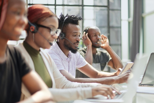 Bella donna afroamericana sorridente che lavora nella call center con la squadra varia