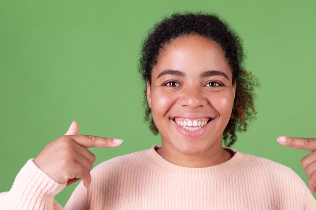 Bella donna afroamericana sulla parete verde allegro sorridente punto di indice sui denti bianchi sorriso