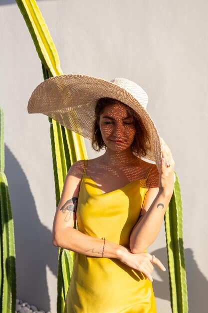 Bella donna alla moda attraente in vestito giallo e cappello di paglia dalla parete