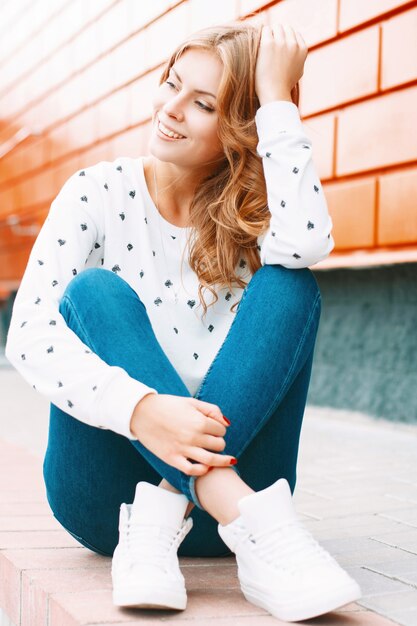 Bella donna alla moda che si siede vicino al muro colorato