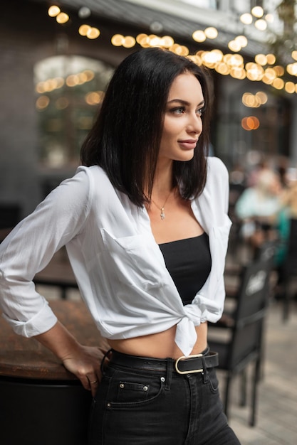 Bella donna alla moda in abiti casual eleganti con una camicia bianca con top nero e jeans in città