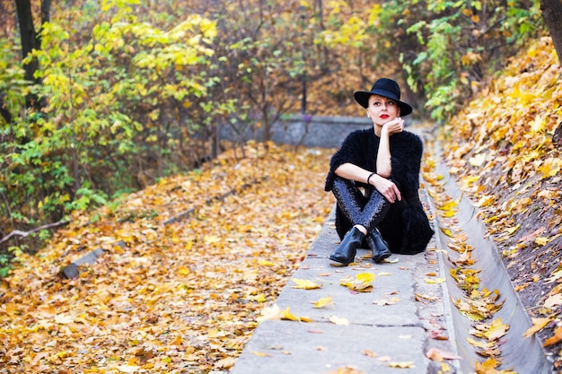 Bella donna alla moda in un cappello nero nella sosta di autunno