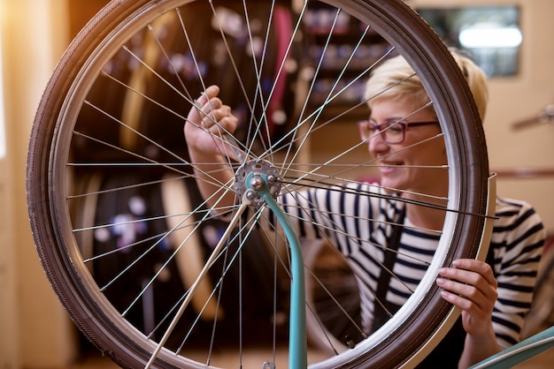 Bella donna allegra che stringe le viti della ruota di bicicletta nel garage.