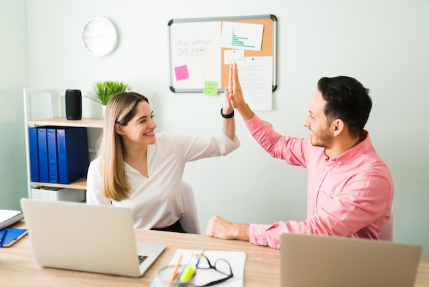 Bella donna allegra e bell'uomo che danno il cinque e sorridono dopo aver terminato il loro lavoro in ufficio. Felici i colleghi che festeggiano