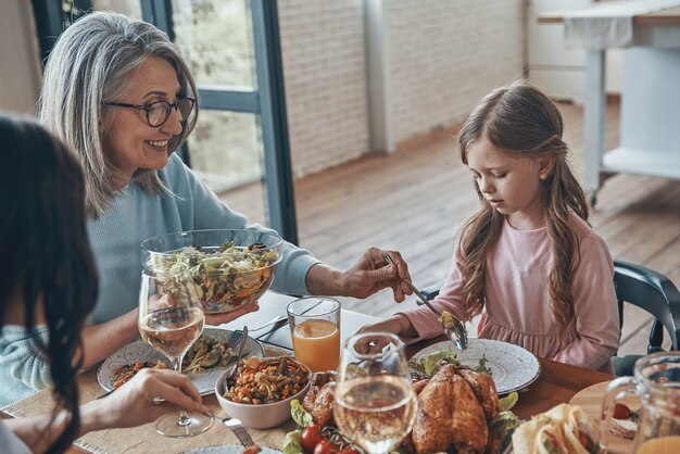 Bella donna anziana che mette insalata per la bambina mentre cena insieme