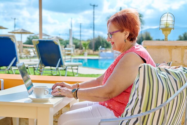 Bella donna anziana in età pensionabile seduta all'aperto con il computer portatile