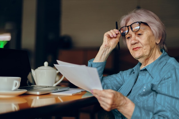 Bella donna anziana matura seduta in un caffè con una tazza di caffè e un computer portatile Stile di vita inalterato