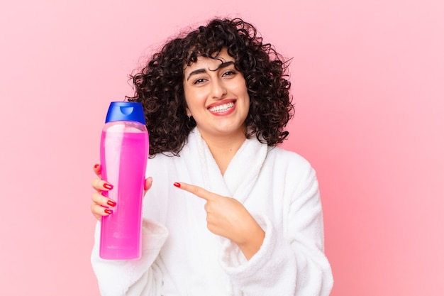 Bella donna araba che indossa accappatoio e tiene in mano una bottiglia di shampoo