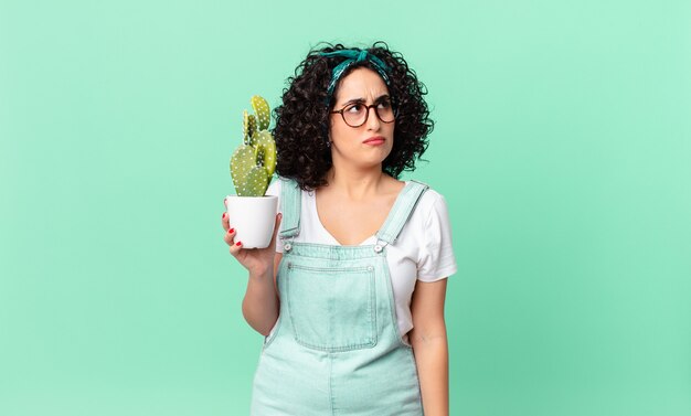 Bella donna araba che si sente triste, sconvolta o arrabbiata e guarda di lato e tiene in mano un cactus in vaso