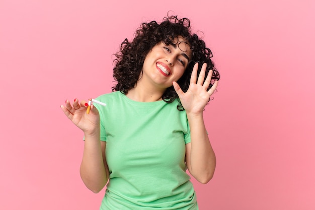 Bella donna araba che sorride felicemente, agitando la mano, accogliendoti e salutandoti. concetto di non fumare