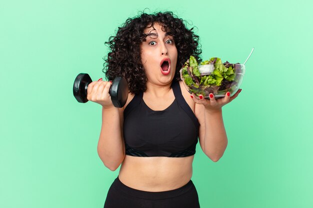 Bella donna araba con un manubrio e un'insalata. concetto di fitness