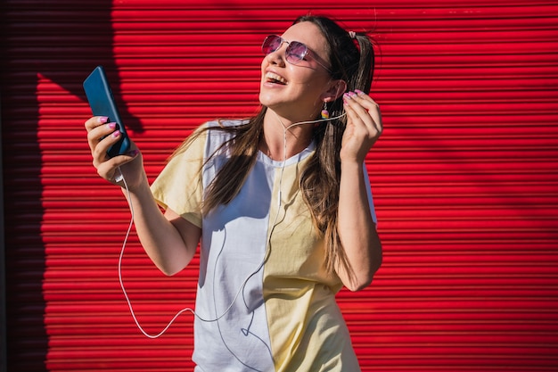 Bella donna ascoltando musica con il suo smartphone su sfondo rosso.